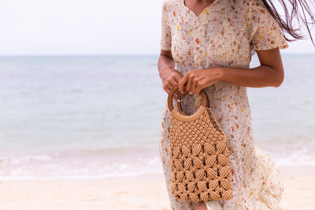 close shot woman light summer flying dress holding knitted bag beach sea background